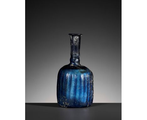 A SAPPHIRE BLUE TRANSPARENT GLASS BOTTLE VASEIran, 10th century. Rising from a concave foot to a bulbous body molded with sli