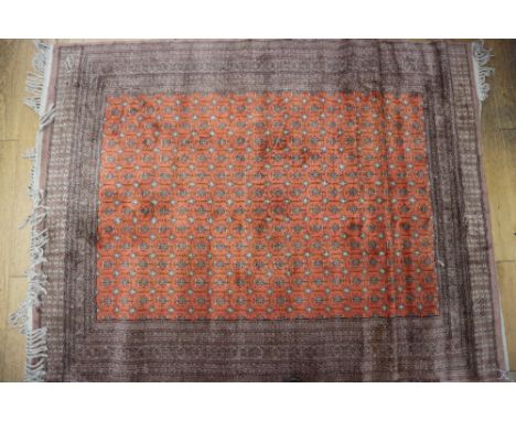 A cotton pile rug of traditional design on an orange ground and multi-bordered in shades of fawn, black and natural, 70" x 54