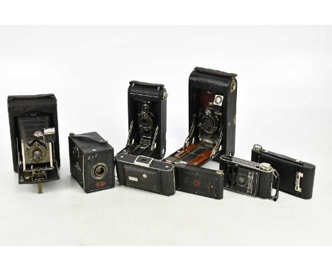 A collection of eight vintage cameras, predominantly Kodak, with manuals. 