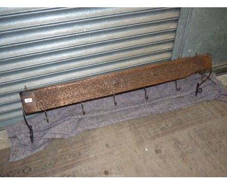 A rustic Indian carved wall shelf/coat rack, having wrought iron scroll work wall fixings, 55" long. 