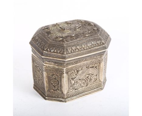 An Indian white metal trinket box of canted form, with scrolled and engraved bird and floral decoration, the lid surmounted b