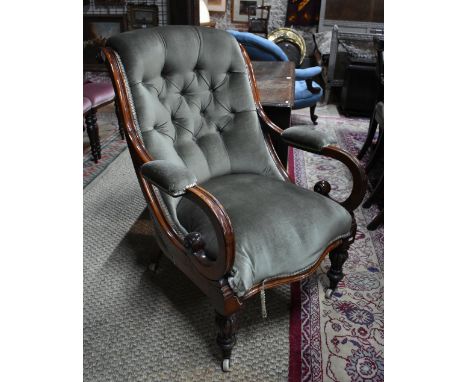 A Victorian mahogany framed scroll armchair with button upholstery, raised on moulded front legs to ceramic castors