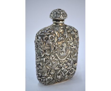 A US unmarked white metal hip flask, richly embossed with floral and foliate designs and with crest and motto 'Je Tiens Ferme
