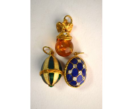 Three various charms including green and yellow enamel egg, blue enamel and white paste egg, and amber and white paste helmet