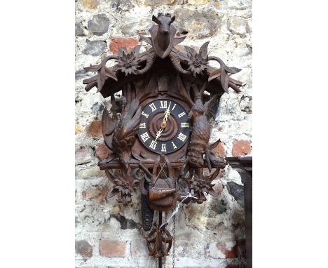 A late 19th century Black Forest cuckoo clock, the case decorated with carved game and flower heads, the gabled top centred b