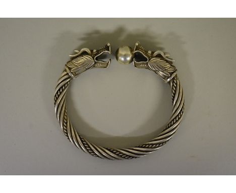 An Oriental white metal torque bangle, having dragon and pearl finials. 
