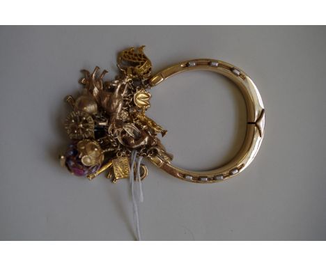 An unmarked horseshoe hinged bangle, having nineteen various charms attached, 92.8g all in. 