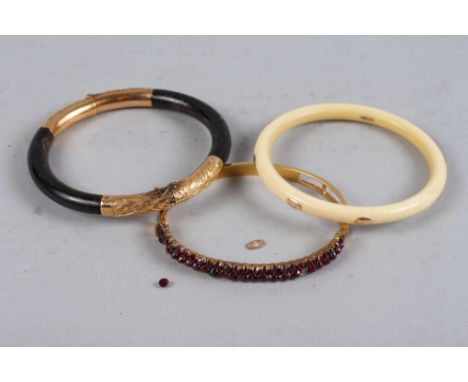 A Chinese yellow metal and ebonised hinged bangle, an ivory bangle with yellow metal mounts, and a yellow metal and garnet hi