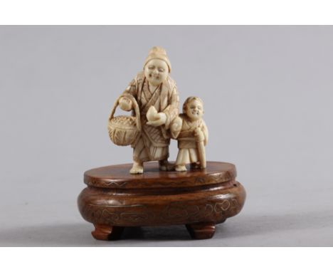 An early 20th century carved ivory figure group/netsuke woman and child, 2" high, on hardwood base 