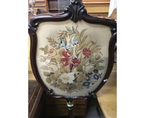 A early Victorian mahogany fire screen the shield centre inset with a floral tapestry attached to brass and mahogany pole ter
