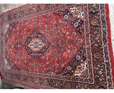 A Quality hand knotted wool carpet with a central blue medallion on a red floral field with a patterned boarder. Size 3Mx1.95