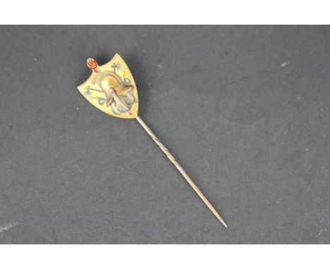 A 19th century yellow metal stick pin, the unusual shield shaped terminal with applied Grecian military helmet and enamelled 