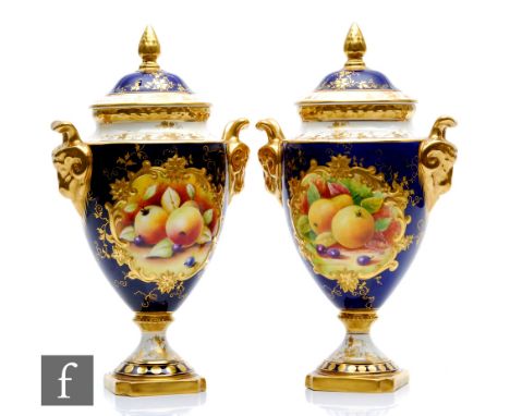 A matched pair of Coalport pedestal vases each decorated with hand painted cartouche panels of fruit against a blue ground, t