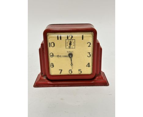 An American Gilbert Art Deco tin plate red enamelled alarm clock with enamelled dial and stylised Deco numerals, with subsidi
