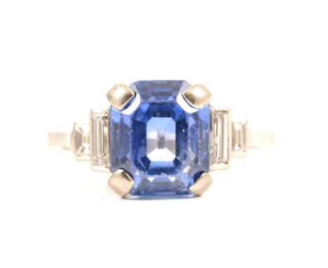 A sapphire ring, the emerald cut stone 8.8x7.5mm four claw set in an all white metal mount with two baguette cut diamonds in 