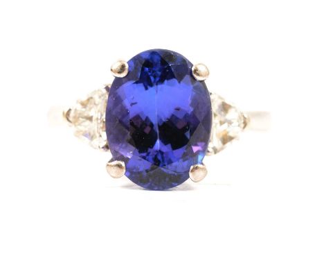 A tanzanite and diamond three stone ring, the oval mixed cut tanzanite 11.3x8.5mm four claw set with a triangular step cut di