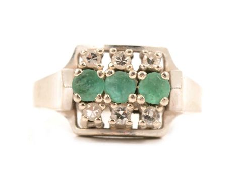 A contemporary emerald and diamond ring, three circular cut emeralds claw set horizontally with three diamonds set in raised 