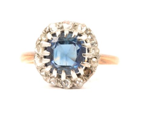 A sapphire and diamond cluster ring, the cushion cut sapphire surrounded by thirteen rose cut diamonds (one missing), yellow 