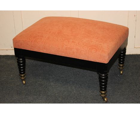An upholstered rectangular stool with ebonised frame and turned legs on brass terminals and castors