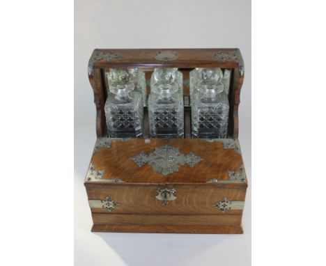 A Victorian metal mounted oak tantalus with three cut glass spirit decanters, over a cigar box, with secret games drawer with