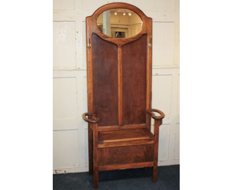 An oak effect hall stand, the raised panel back with oval mirror and two coat hooks above a bench with hinged box seat and ar