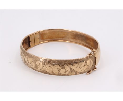 A 9 ct gold hinged bangle, decorated with foliate scroll engraving, 63 mm x 57 mm internally, 15 g