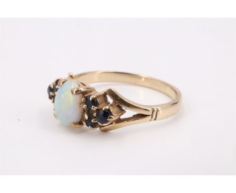 An opal and sapphire ring, comprising an oval opal cabochon of approx 7 mm x 5 mm, claw-set between trios of small sapphires 