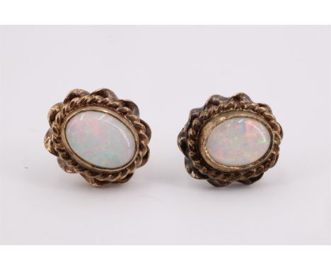 A pair of opal and 9 ct gold stud earrings, each being a 6.5 x 5 mm cabochon in a rubbed over setting surrounded by two varyi