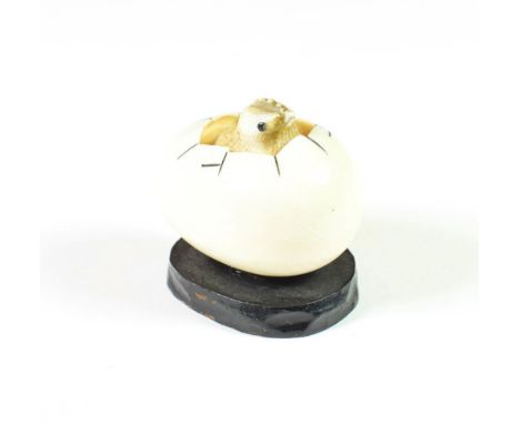 A Japanese meiji period carved ivory netsuke formed a chick hatching from an egg, signed and later mounted on a wooden plinth