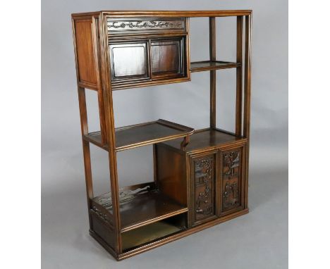 A Chinese hongmu display cabinet, c.1910, with an arrangement of cupboards and a drawer carved in high relief with figures an