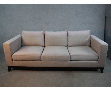 A contemporary three seater sofa, upholstered in light grey fabric, with angular arms, loose seat and back cushions, on an eb