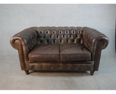 A late 20th century brown leather two seater Chesterfield sofa, with buttoned back and arms and two loose seat cushions, on t