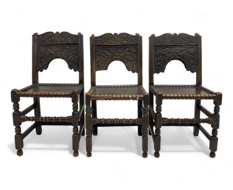 Set of three 18th century carved oak back stools, the cresting rail carved with scrolling foliate motifs over an arched panel