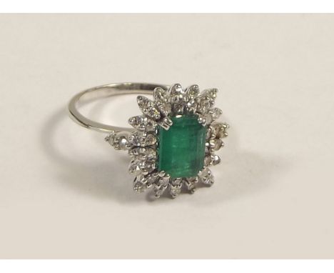 EMERALD RING. An 18ct. white gold emerald &amp; diamond cluster ring. Size O. Setting size 1.5 x 1.3cm.