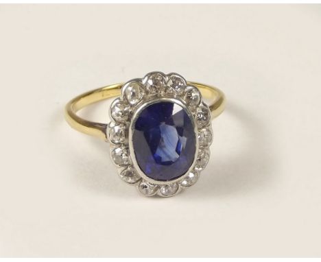 DIAMOND RING. An 18ct. gold synthetic sapphire &amp; diamond cluster ring. The old synthetic sapphire 10 x 7 x 5mm, surrounde