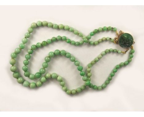 JADE BEADS. A double strand of pale celadon jade beads, the gold clasp with bird-carved jade inset. (Note: although the clasp