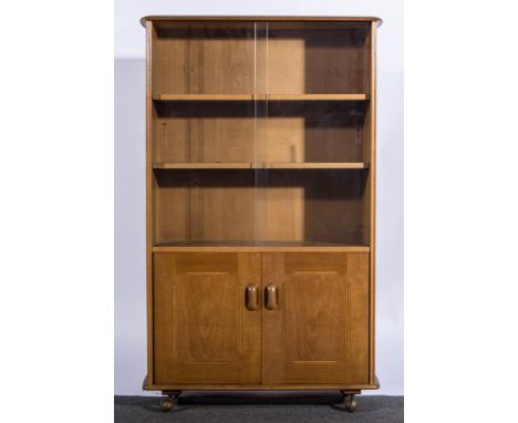 An Ercol blonde beech bookcase cabinet, sliding glass doors enclosing two adjustable shelves,pair of cupboards, raised on cas