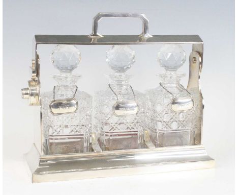 An Edwardian silverplated three-bottle tantalus, the hinged top with locking mechanism (no key), enclosing three hobnail cut 