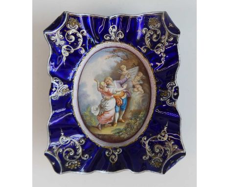 An early 20th century Austrian enamel on metal decorated dish, the border of raised and shaped form, the central oval decorat