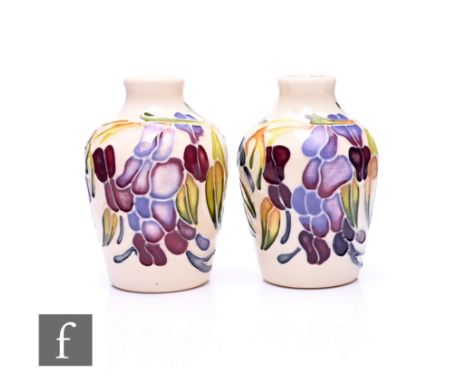 Emma Bossons - Moorcroft Pottery - A pair of miniature vases, tube line decorated with trailing wisteria flowers in tonal pur