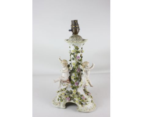 A continental porcelain table lamp, decorated with winged cherubs amidst roses, on shaped scroll base, arrow mark to base, 35