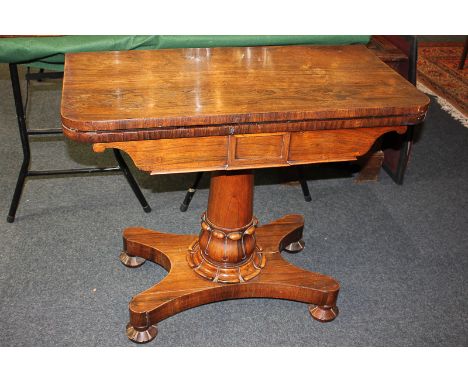 A 19th century rosewood card table with fold-over rectangular top, on carved pedestal and platform base with four carved bun 