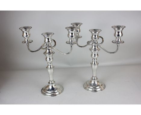 A pair of silver plated three-light candelabra with vase shape sconces, twin scroll branches, on baluster stems and circular 