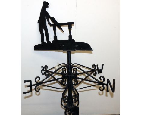 Black painted metal weather vane, with a carpenter sawing at a bench pointer on wrought metal scroll bracket, W77cm H113cm 