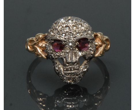 A Gothic ruby and diamond skull ring, white metal face, pave encrusted with old and rose cut diamond accents, inset pinky red