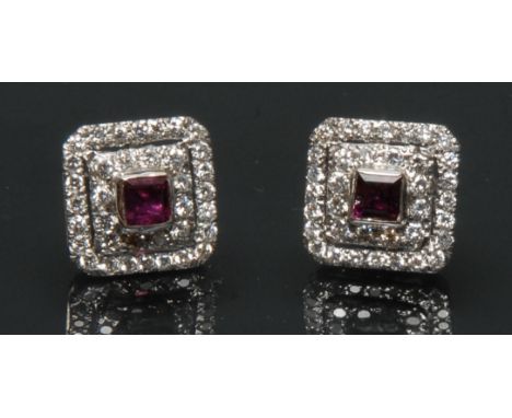 A pair of ruby and diamond cluster earrings, each with a central baguette cut red ruby, surrounded by a double stepped band o