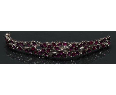 A ruby and diamond cocktail bracelet, tapering floral body pave encrusted with fifty three oval pinky red rubies and over eig