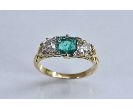 A diamond and emerald trilogy ring, central cushion cut pale green emerald approx 0.62ct, flanked by a single old cut diamond