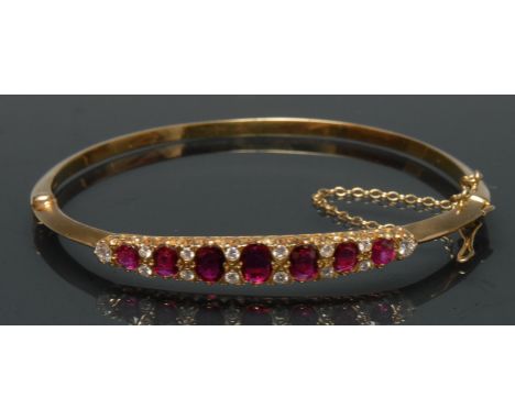 A ruby and diamond hinge bangle, seven graduated red and pink rubies, ranging from approx 0.20ct to 0.55ct, each divided by a