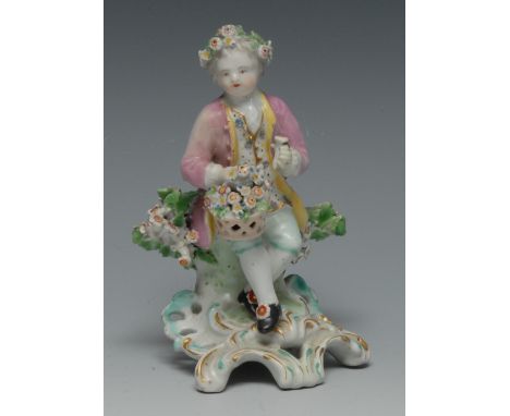 A Derby Patch Mark figure, of a boy seated wearing a floral chaplet and holding a basket of flowers, before bocage, pierced s